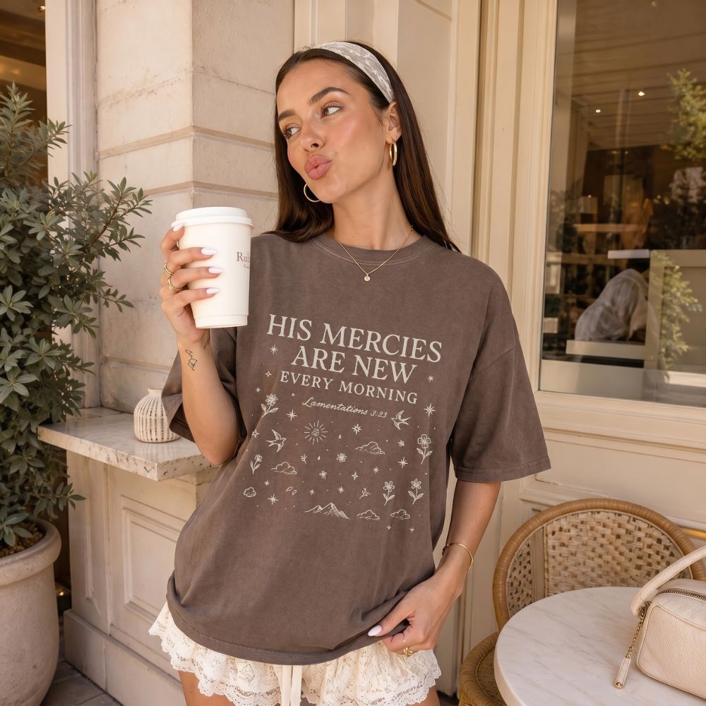 Woman wearing a t-shirt with a religious quote, holding a coffee cup outdoors.
