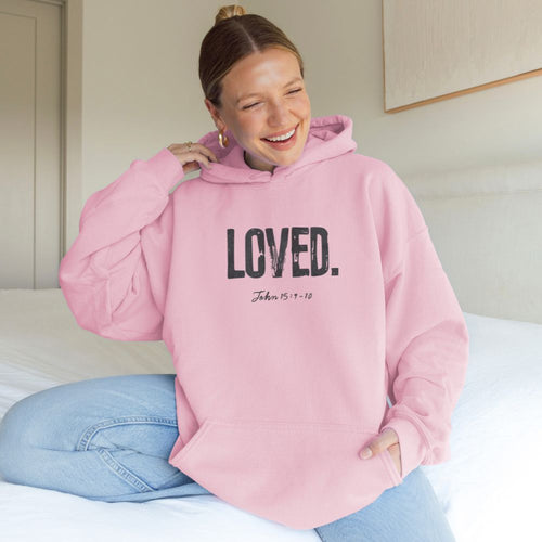 Person wearing a pink hoodie with 'LOVED' text, sitting on a bed.