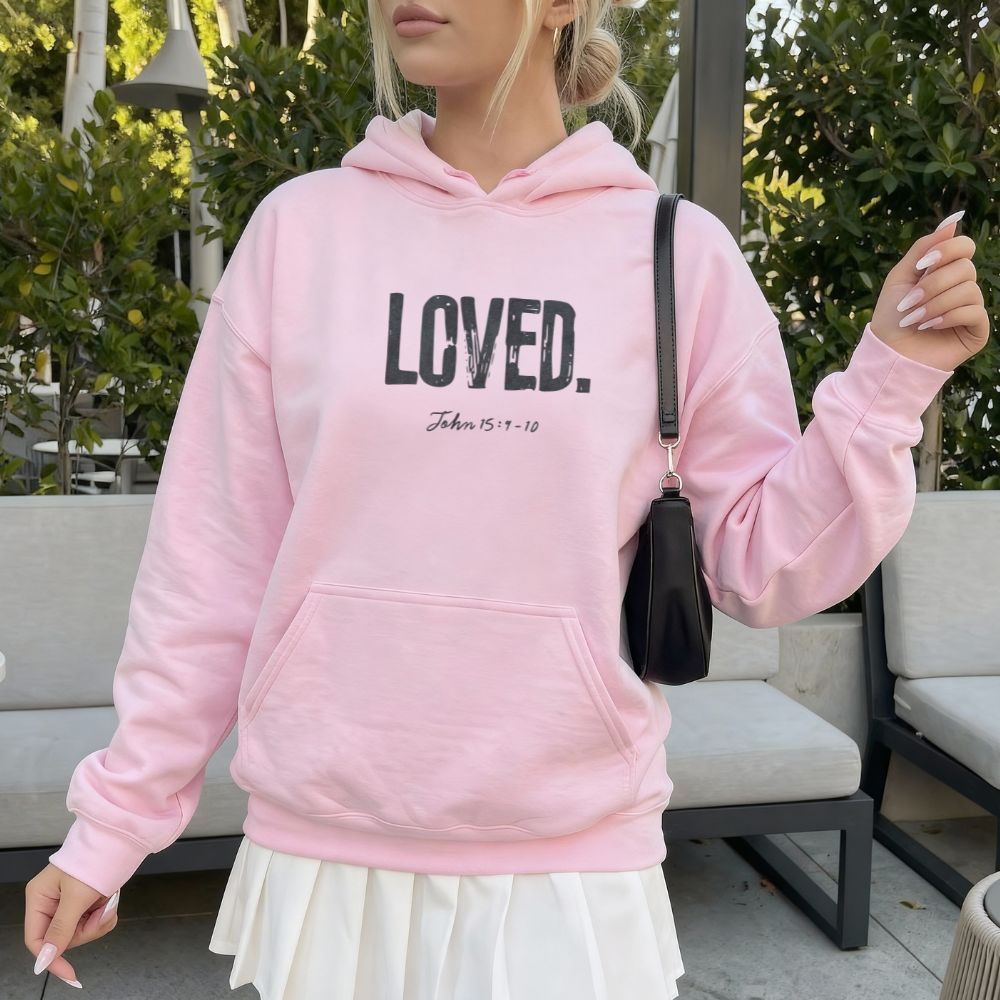 Person wearing a pink hoodie with 'LOVED' text, standing outdoors.
