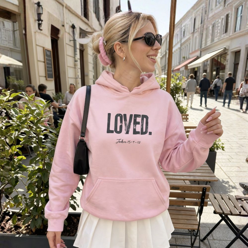 Woman wearing a pink hoodie with 'LOVED' text on a city street.