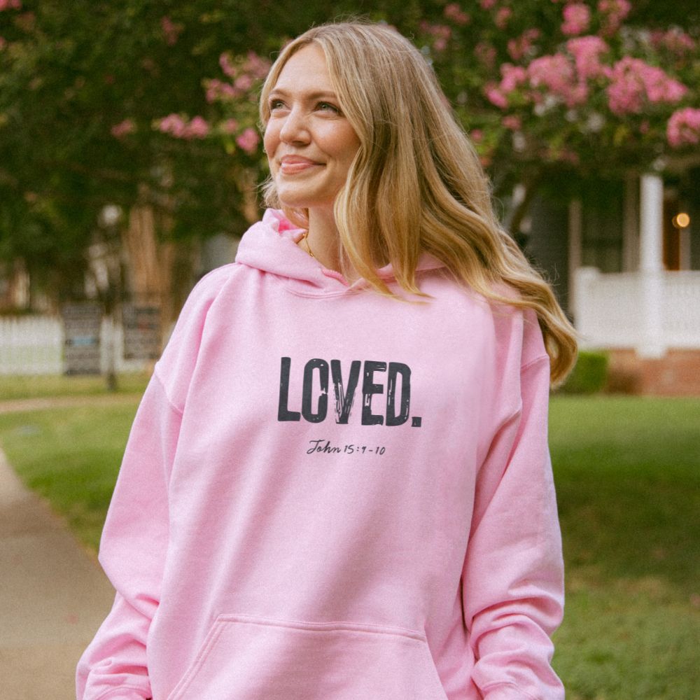 Woman wearing a pink hoodie with 'LOVED' text outdoors.