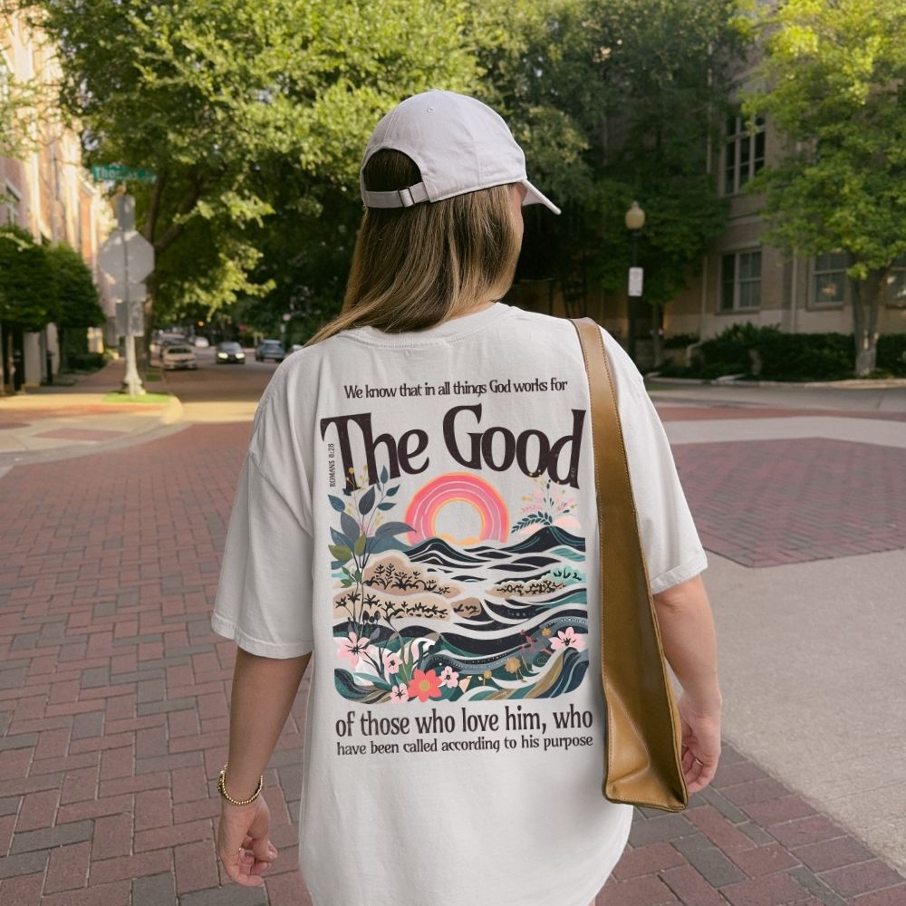 Person wearing a white t-shirt with a graphic design and text, walking on a sidewalk.