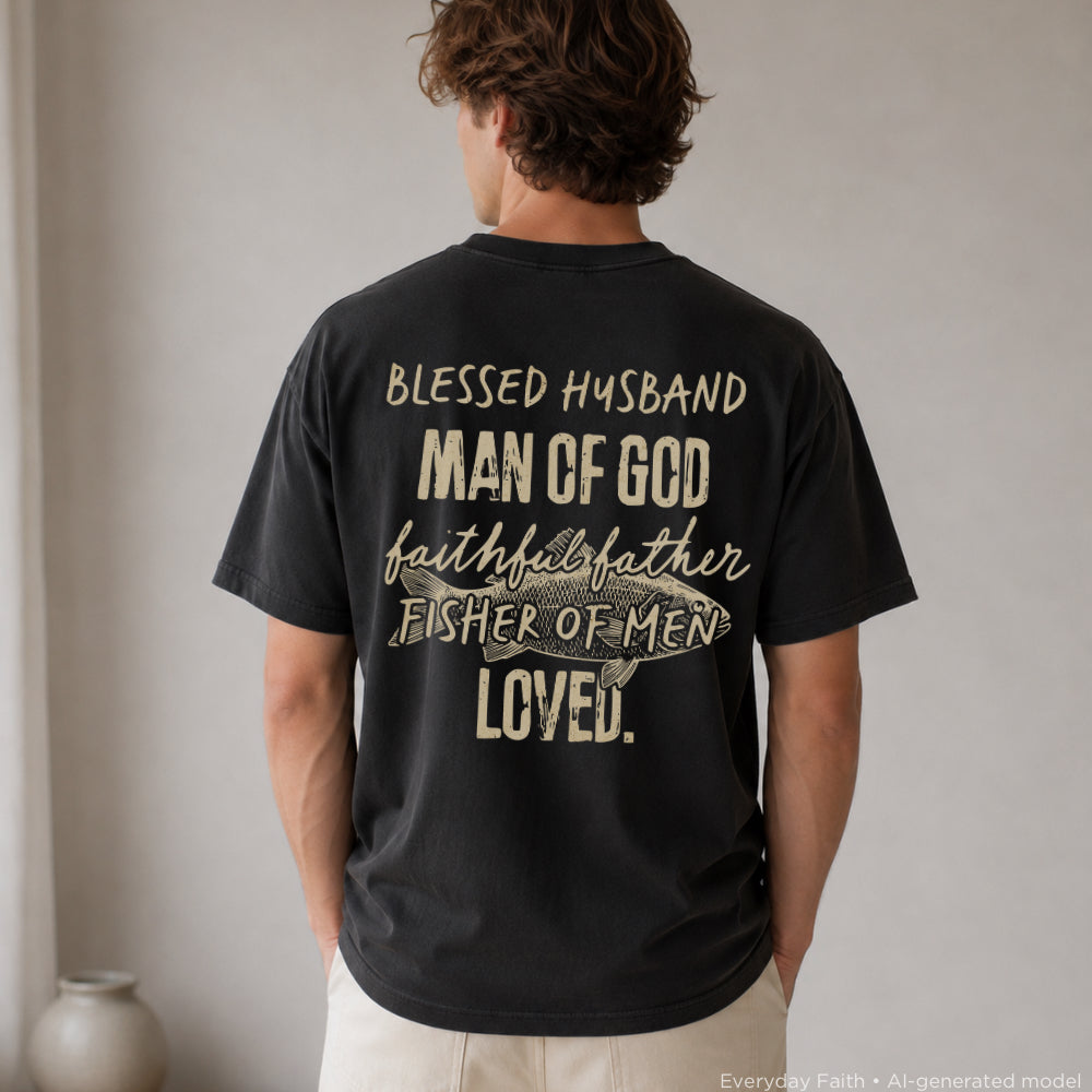 A man viewed from behind wearing a black Everyday Faith t-shirt with a beige graphic print on the back that reads 'BLESSED HUSBAND MAN OF GOD faith faithful father FISHER OF MEN LOVED.'.