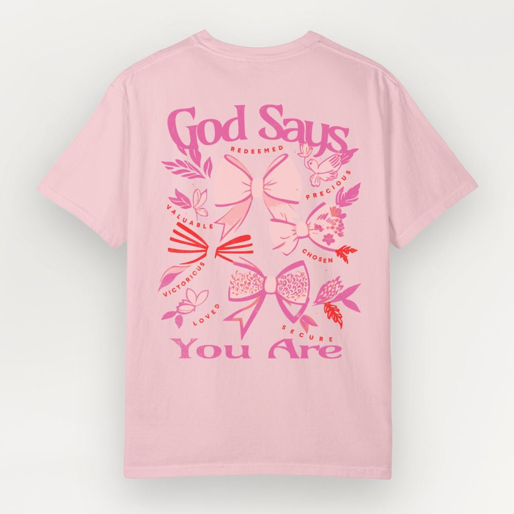 Pink Everyday Faith heavyweight t-shirt with decorative text and graphics on a white background. Graphic features coquette bows and words ‘God Says You Are’