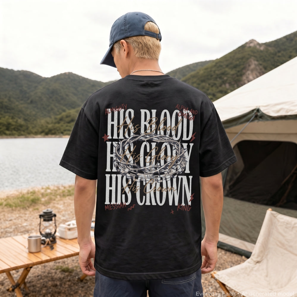 A man viewed from behind wearing a black Everyday Faith graphic t-shirt with a large white and red design on the back, standing in a campsite setting with a lake, mountains, and a tent in the background.