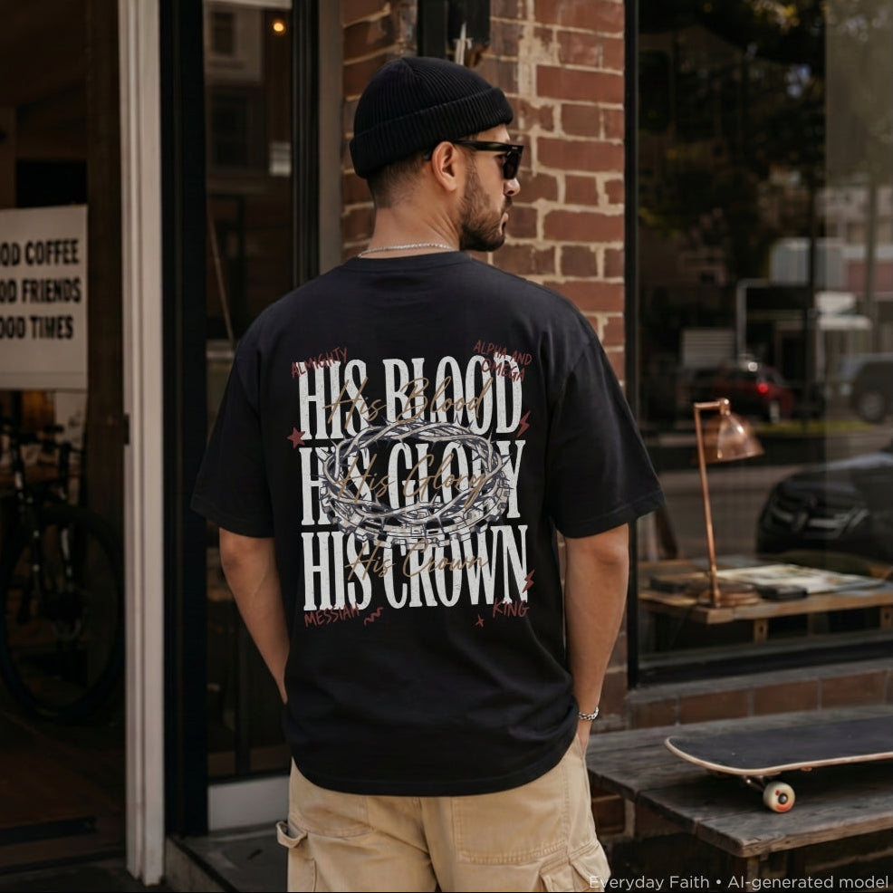 A man wearing a black Everyday Faith t-shirt with a large white graphic text print reading 'HIS BLOOD HIS GLORY HIS CROWN' on the back, standing in front of a brick storefront.