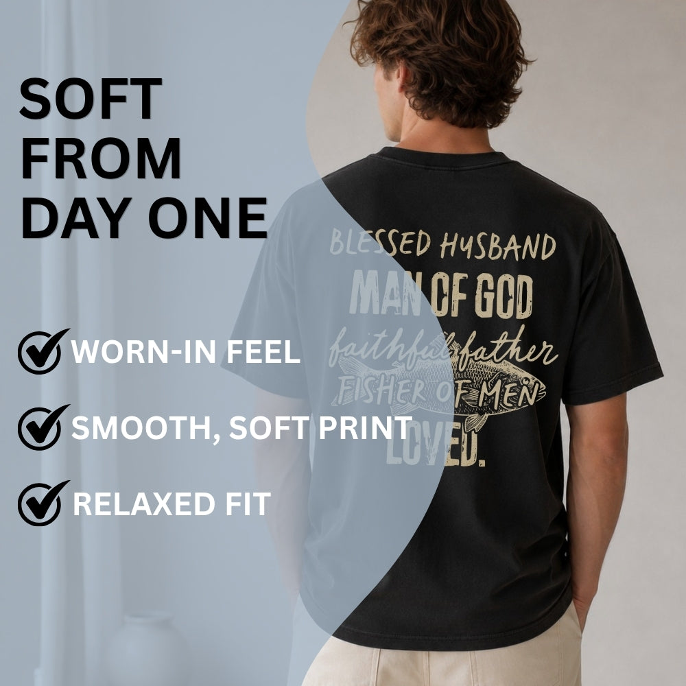 A man shown from the back wearing a black graphic T-shirt with white and beige text reading 'Blessed Husband Man of God faith faithful father Fisher of Men Loved.' There is large marketing text on the left saying 'SOFT FROM DAY ONE' and bullet points about worn-in feel, smooth soft print, and relaxed fit.