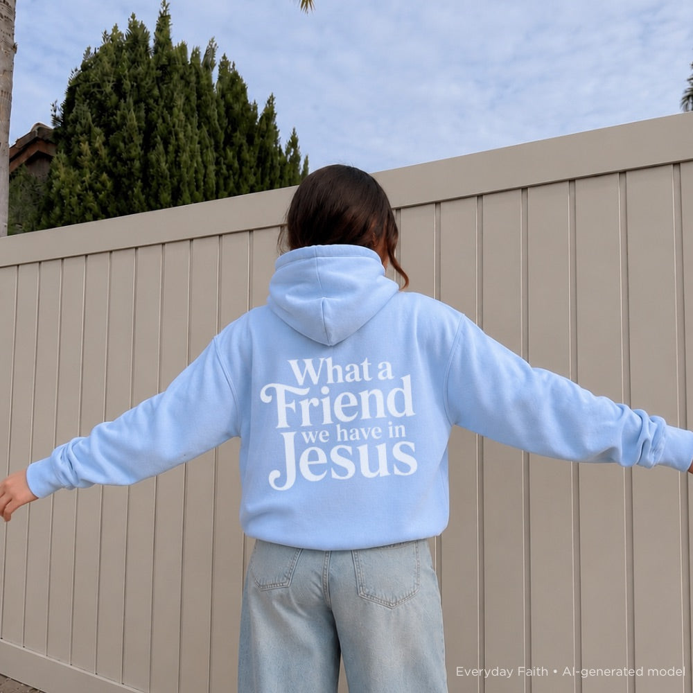 Person wearing a light blue Everyday Faith hoodie with ‘What A Friend We Have In Jesus’ text, standing against a beige fence.