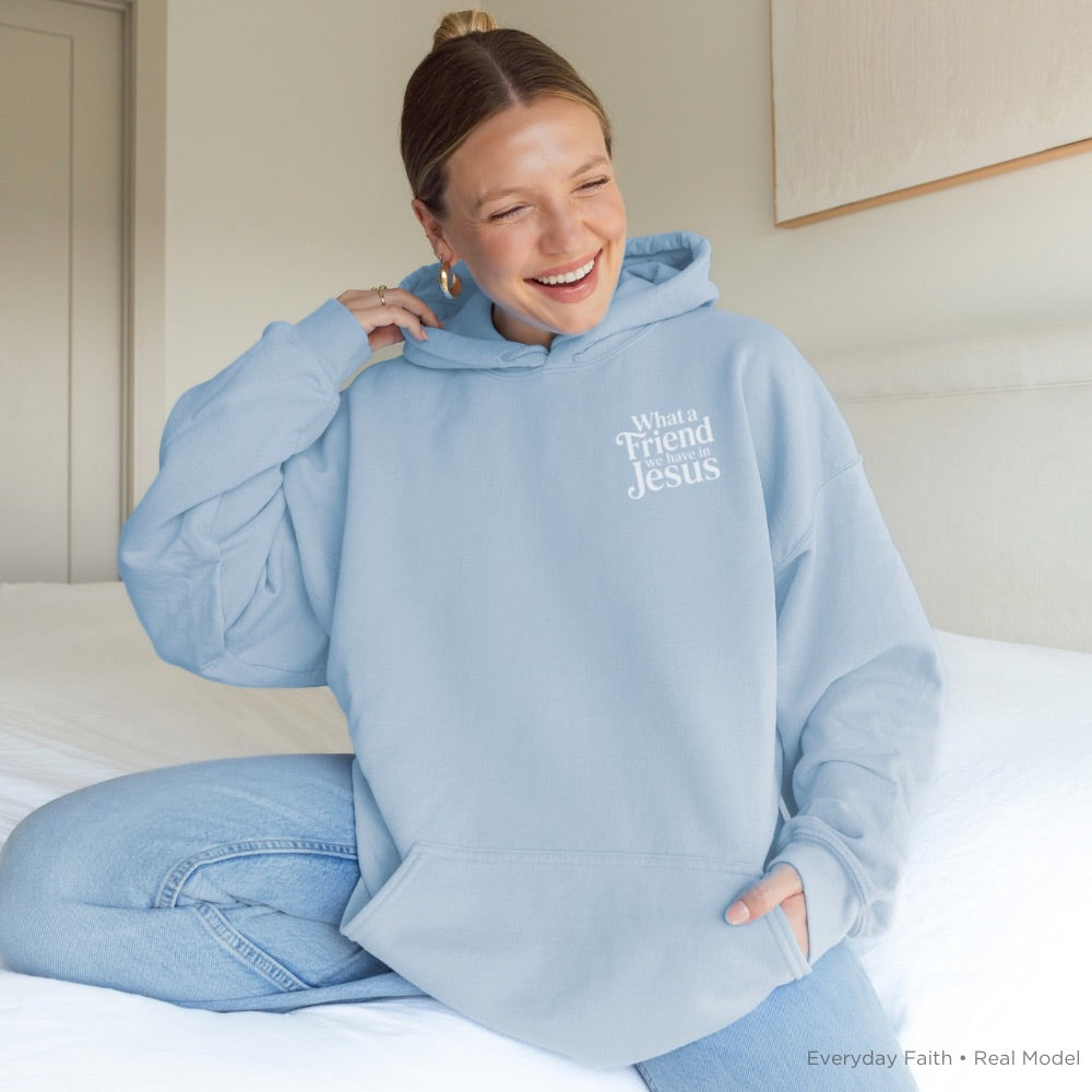 Person wearing a light blue Everyday Faith hoodie with text that says ‘What a friend we have in Jesus’ sitting on a bed.