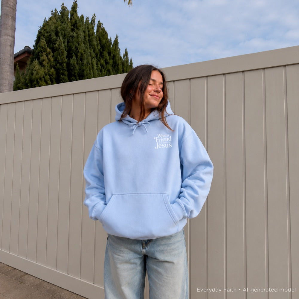 Person wearing a light blue Everyday Faith hoodie with ‘What a friend we have in Jesus’ text, standing against a beige fence.