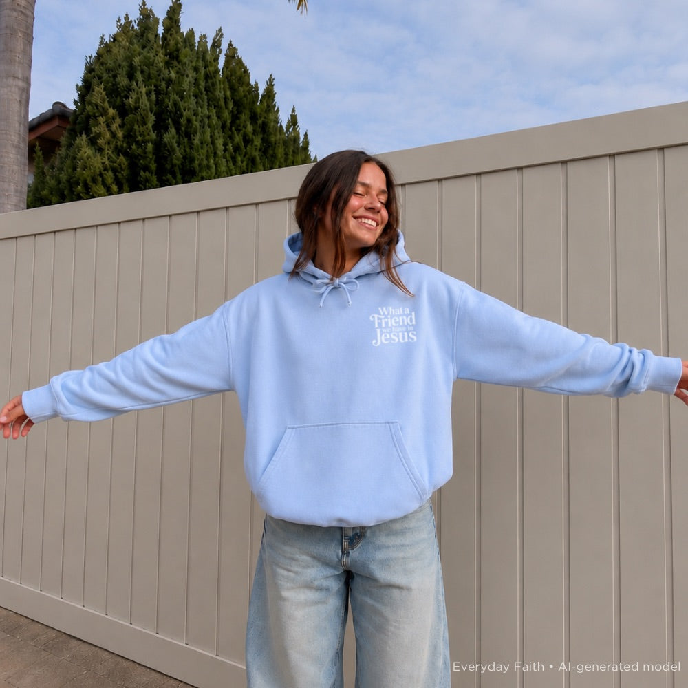 Person wearing a light blue Everyday Faith hoodie with ‘what a friend we have in jesus’ text, standing outdoors with a neutral background.