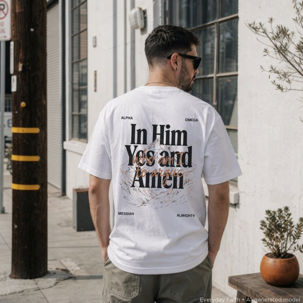 A man viewed from behind wearing a white Everyday Faith graphic t-shirt with 'In Him Yes and Amen' printed in black and brown on the back, standing outdoors on a sidewalk next to a building.