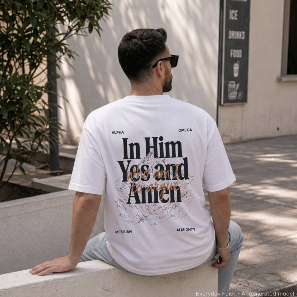 A man wearing a white Everyday Faith graphic t-shirt with 'In Him Yes and Amen' printed on the back, sitting outdoors on a concrete ledge.