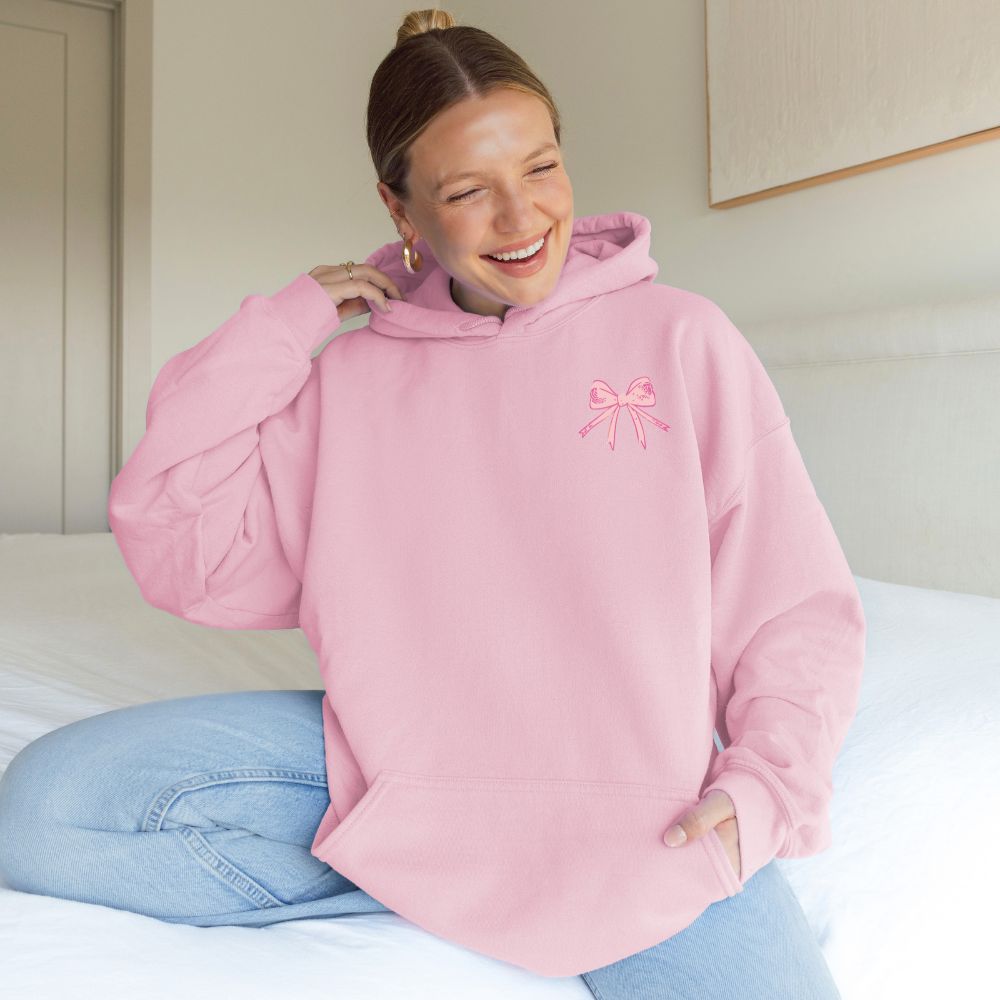Person wearing a pink hoodie with a bow design, sitting on a bed.