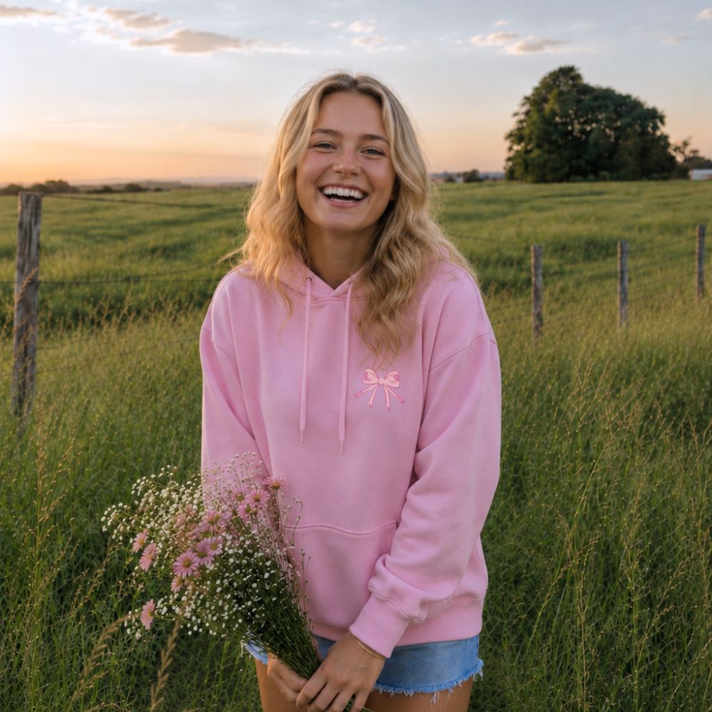 Woman in a pink hoodie standing in a field with a sunset background