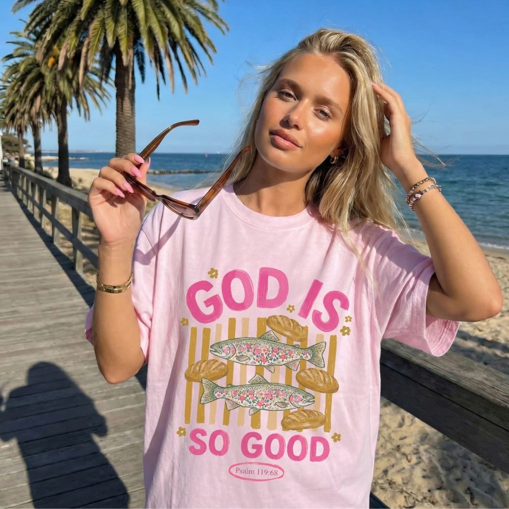 Woman wearing a pink t-shirt with 'God is so good' text on a beach.