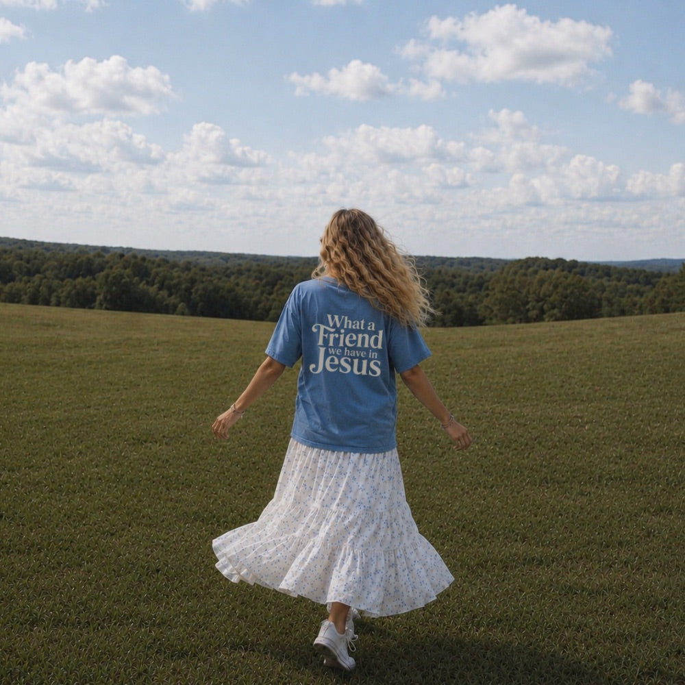 Woman in a blue t-shirt with text walking in a field under a blue sky.