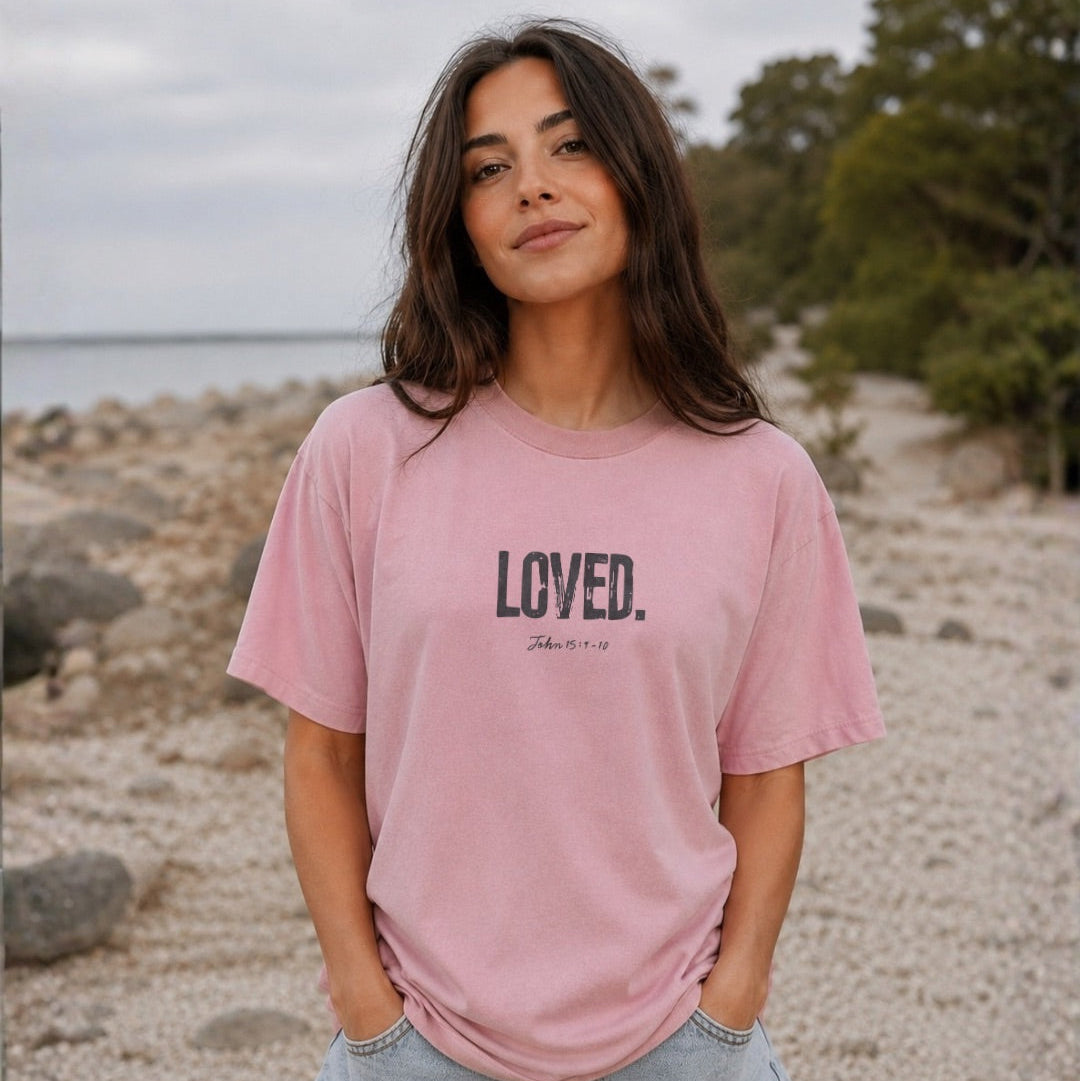 Woman wearing a pink t-shirt with 'LOVED' text on a beach