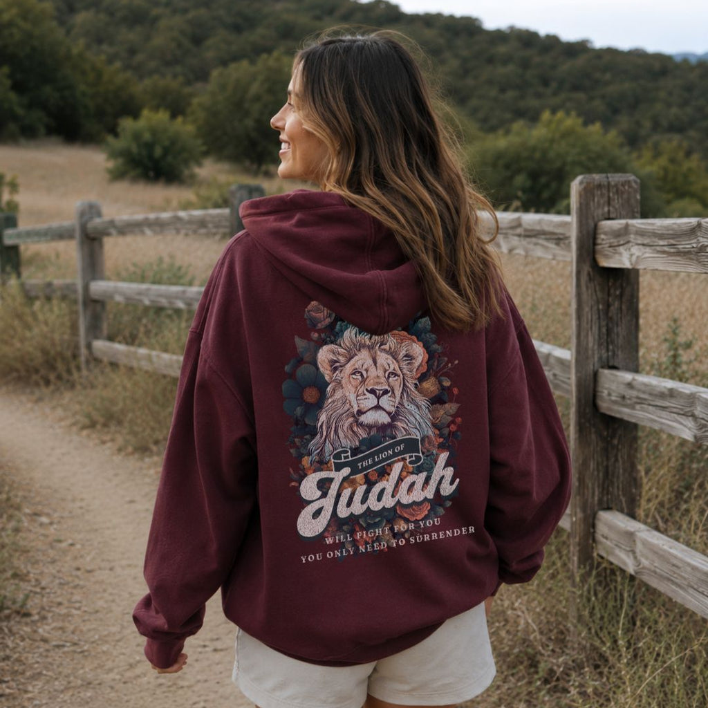 Woman wearing a maroon hoodie with a lion graphic and text, standing in a natural setting.