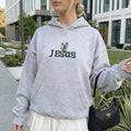 Person wearing a gray hoodie with 'Jesus' printed on it, standing outdoors.
