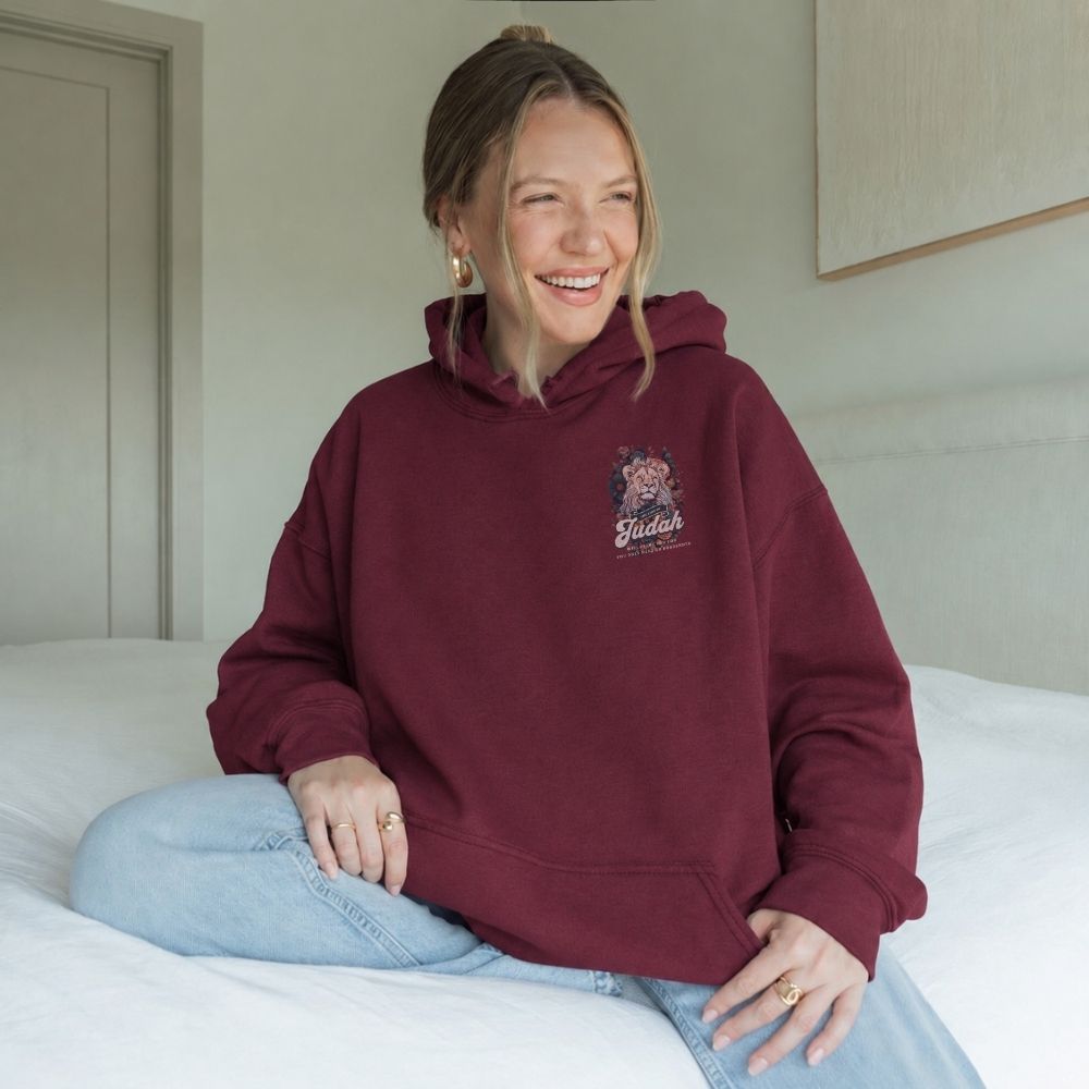 Woman wearing a maroon hoodie with a logo, sitting on a bed.