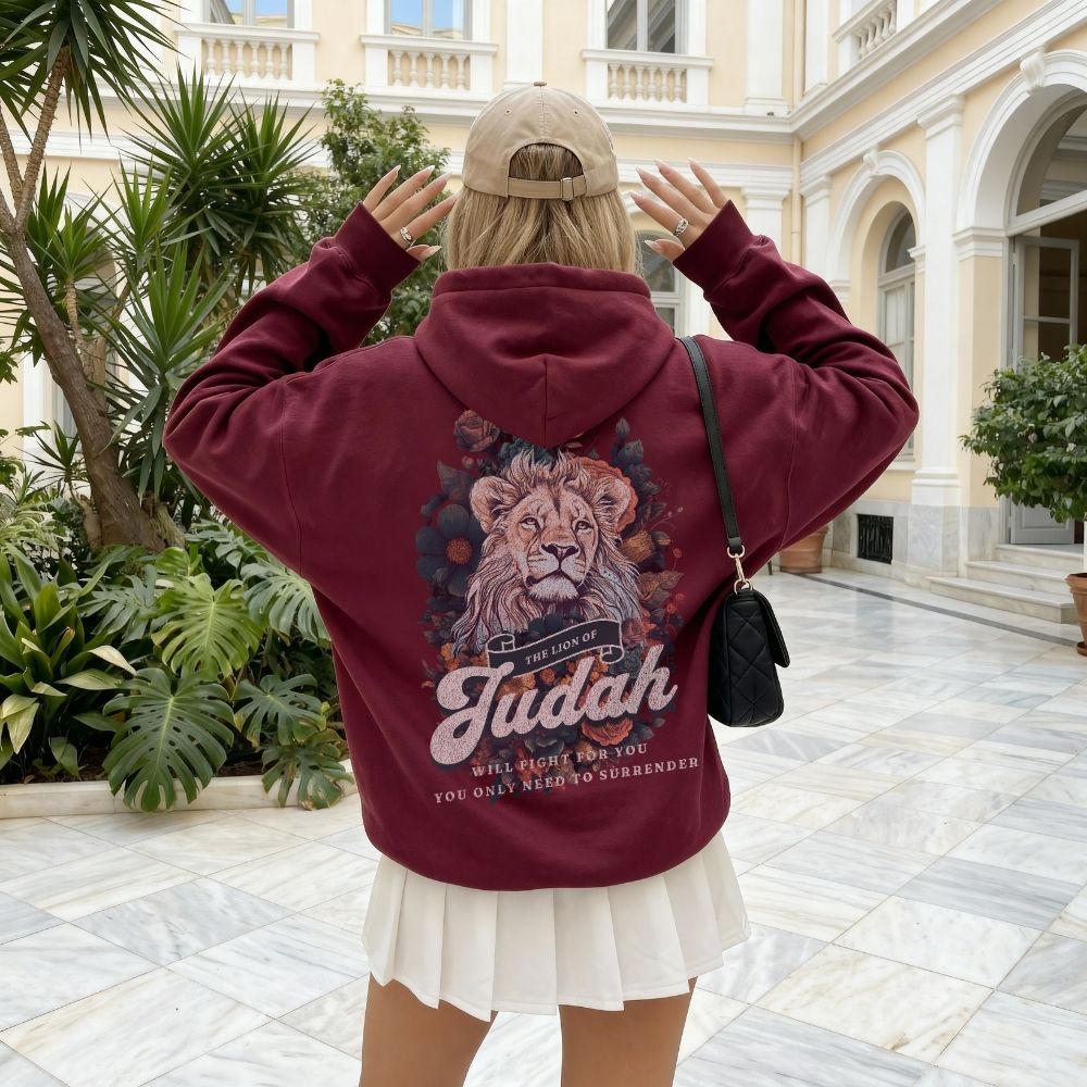 Person wearing a maroon hoodie with a lion graphic and text in an indoor setting with plants and architecture.