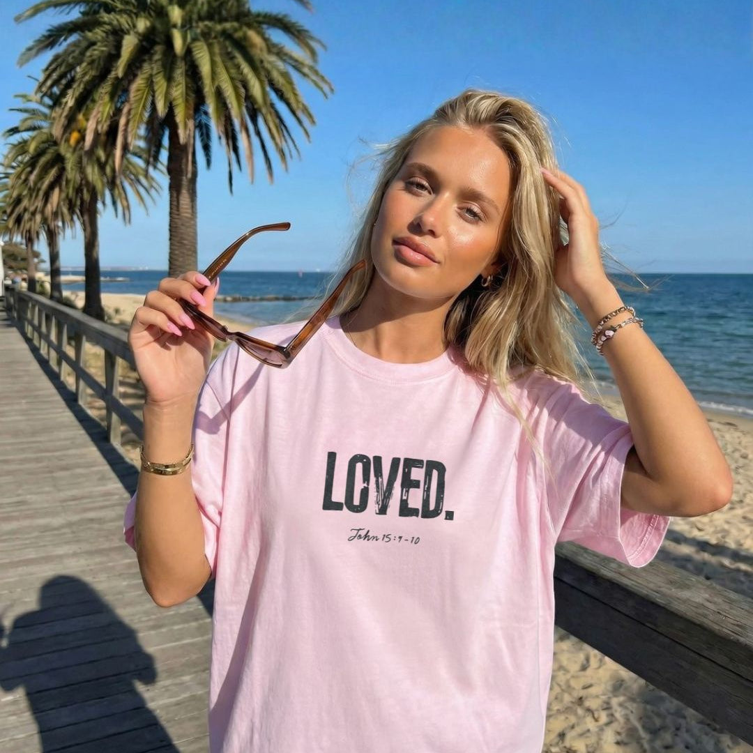 Woman wearing a pink t-shirt with 'LOVED' text at a beach.