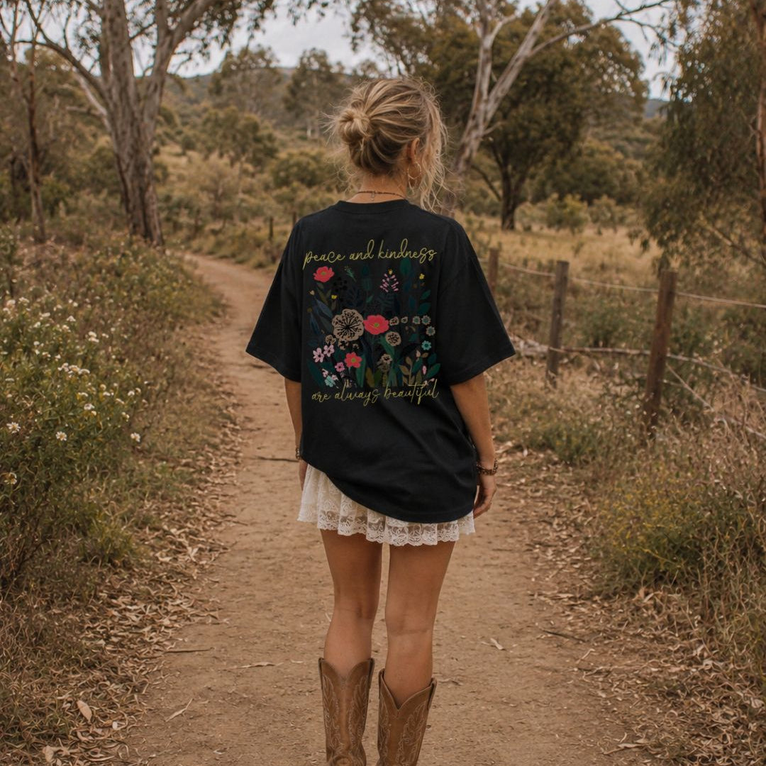 Person walking on a dirt path in a natural setting wearing a black t-shirt with floral designs and text.