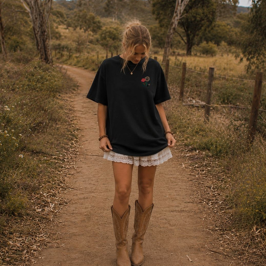 Woman in a black shirt and white skirt with brown boots walking on a dirt path in a natural setting.