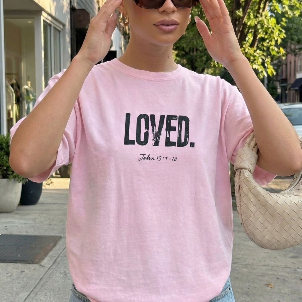 Person wearing a pink t-shirt with 'LOVED' text outdoors.