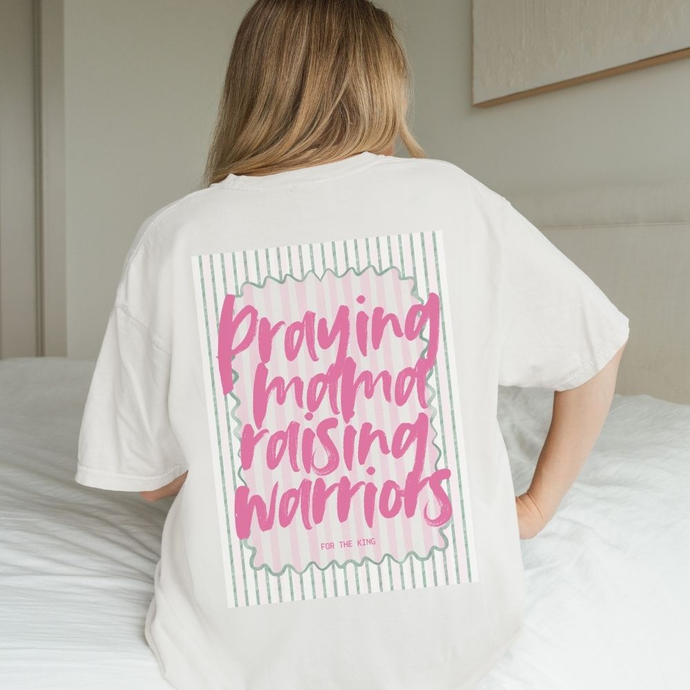Person wearing a white t-shirt with pink text on the back, standing in a bedroom.
