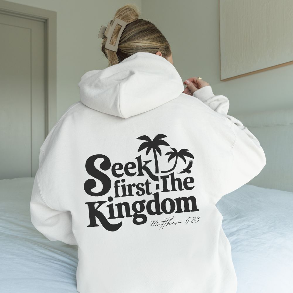 Person wearing a white hoodie with 'Seek first the Kingdom' text on the back, standing in a bedroom.