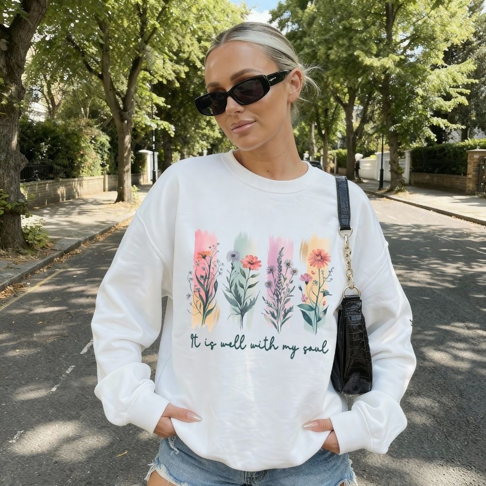 Woman wearing a white sweatshirt with floral designs and text outdoors.