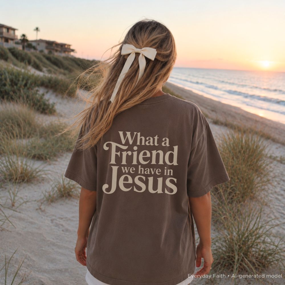Person wearing a brown t-shirt with 'What a Friend we have in Jesus' text on a beach at sunset.