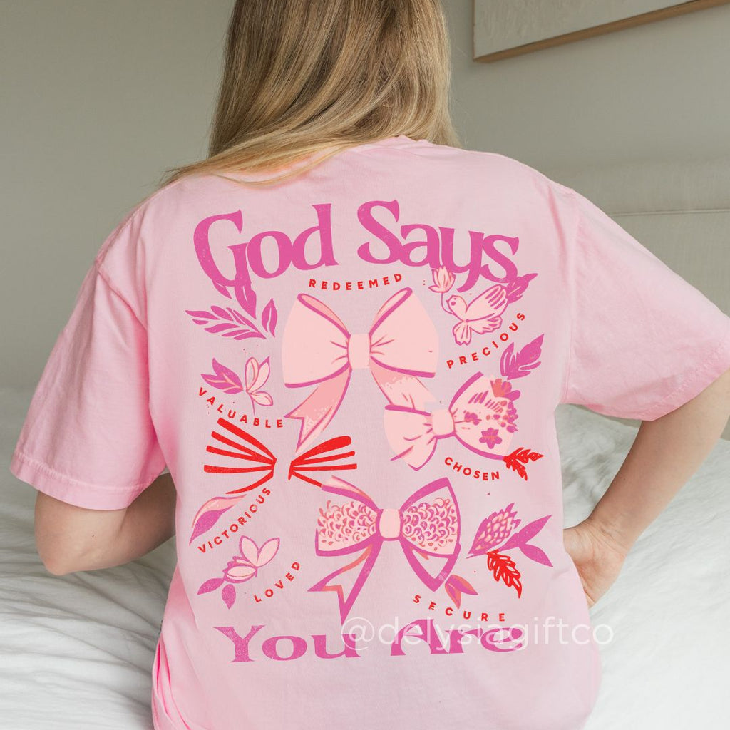 Woman wearing pink God Says You Are Christian t-shirt with bow graphics and uplifting faith affirmations on the back.