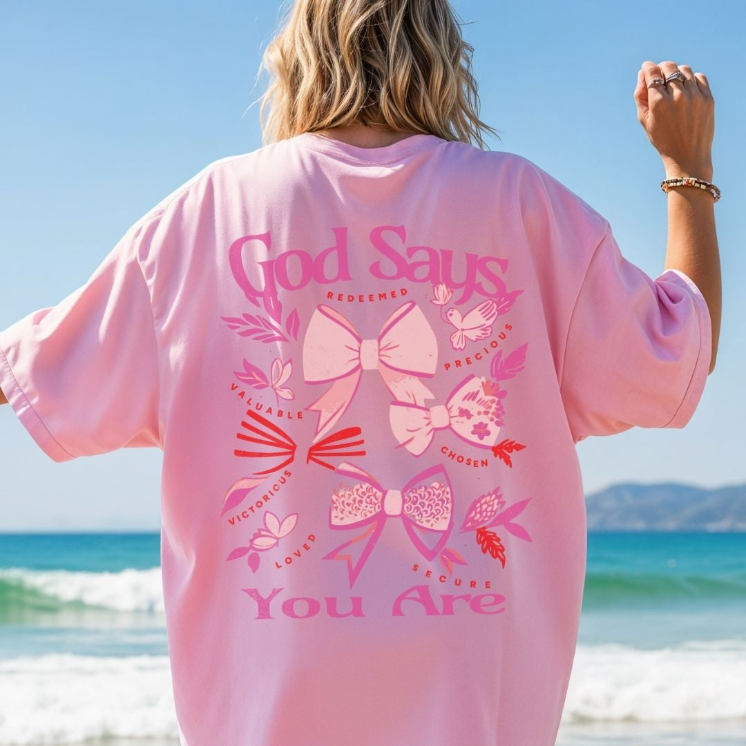 Woman wearing pink God Says You Are Christian t-shirt with bow graphics and uplifting faith affirmations on the back.