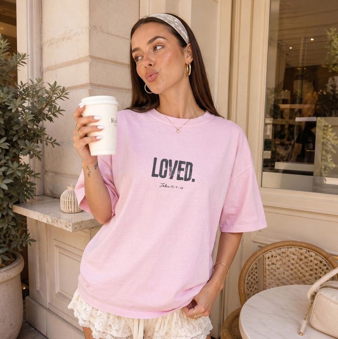 Woman in a pink 'LOVED' t-shirt holding a coffee cup outdoors.